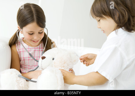 Two children playing doctor, girl listening to teddy bear's heart with stethoscope Stock Photo