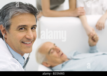 Doctor smiling at camera, senior man lying on couch in background Stock Photo
