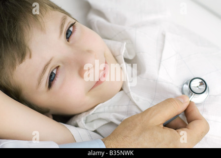 Doctor holding stethoscope on boy's chest, boy smiling at camera, cropped view Stock Photo