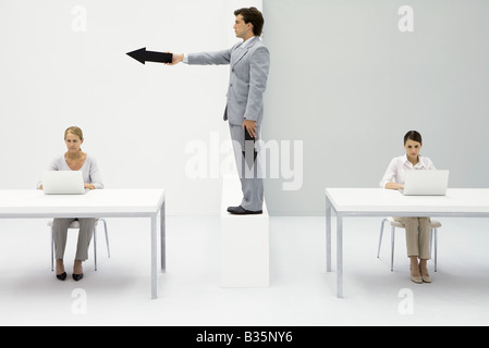 Professional women working in office, man standing between them, pointing arrow Stock Photo