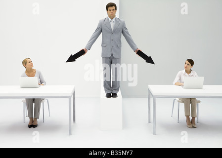 Businessman standing between two female employees, pointing arrows at each of them Stock Photo