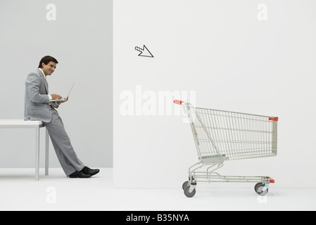 Businessman leaning against desk, shopping online, cursor pointing at shopping cart Stock Photo