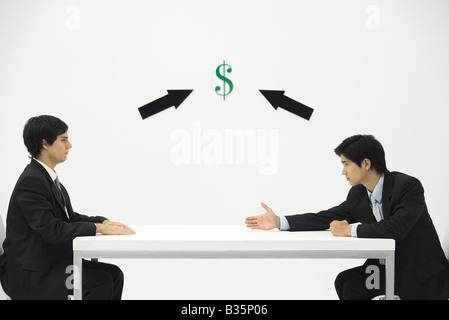 Two businessmen face to face, one reaching to offer his hand, dollar sign and arrows between them Stock Photo