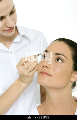 Woman looking up, beautician using tweezers to remove an eyelash Stock Photo