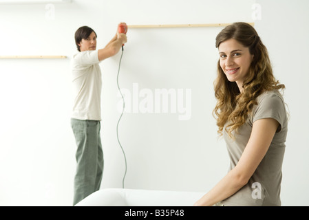 Man attaching thin piece of wood to wall, woman in foreground smiling at camera Stock Photo