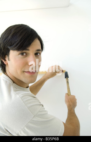 Man nailing thin piece of wood to wall, looking back over shoulder at camera Stock Photo