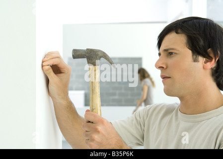 Man hammering nail into wall, woman in background Stock Photo