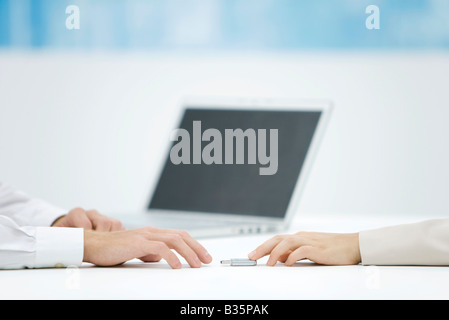 Hand pushing a flash drive across desk to another hand reaching for it Stock Photo