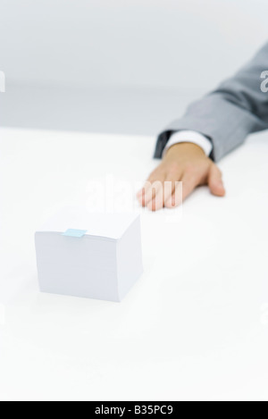 Stack of paper with small adhesive note stuck on it, cropped view of arm nearby Stock Photo