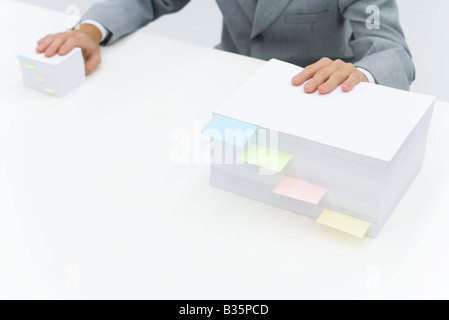 Stacks of paper with adhesive notes dividing them, man putting one hand on each stack Stock Photo