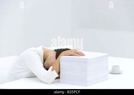 Woman with head down on desk, arm obscuring face, hand on top of stack of paper Stock Photo