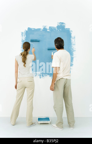 Couple painting wall blue using rollers, rear view Stock Photo