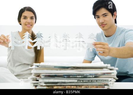 Two young adults holding tree shapes cut out of newspaper, smiling at camera Stock Photo
