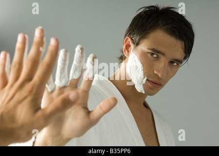 Man with shaving cream on his face and fingers, looking at self in mirror Stock Photo