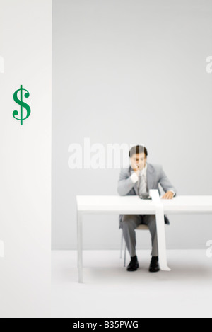 Accountant using adding machine, holding head, dollar sign in foreground Stock Photo