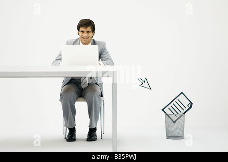 Businessman working on laptop, cursor pointing toward document in wastepaper basket Stock Photo