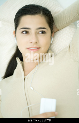 Young woman lying down, listening to MP3 player, high angle view