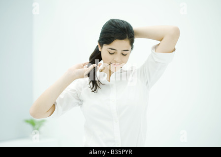 Woman fixing hair, holding hairpin in mouth, looking down Stock Photo