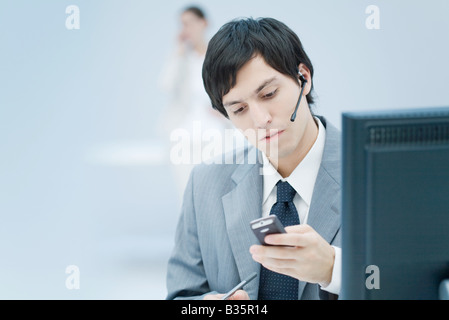Young businessman wearing headset and looking down at cell phone Stock Photo