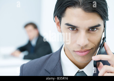Young professional man holding cell phone, smirking at camera, portrait Stock Photo