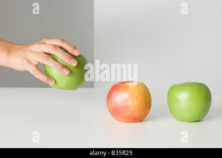 Hand picking up an apple, two other apples sitting in a row, cropped view Stock Photo