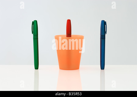 Pens standing upright in a row, the middle pen upside down inside of cup Stock Photo