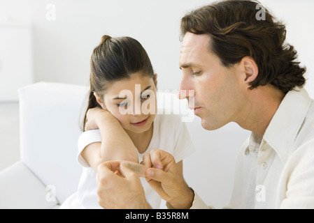 Man putting adhesive bandage on girl, both sitting on couch Stock Photo
