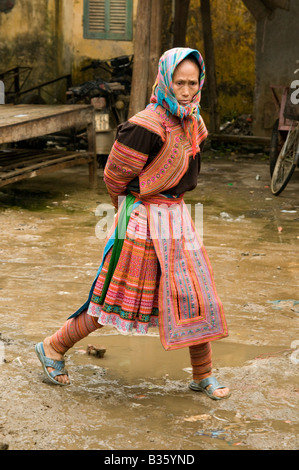 A Flower Hmong women wearing traditional costume steps through the mud at Muong Khuong market North Vietnam Stock Photo