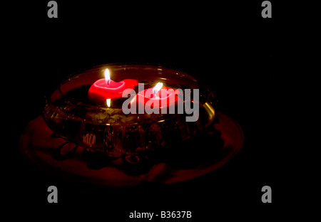 A Bowl holds water and two red floating candles with flame in the dark. Stock Photo