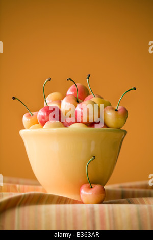 yellow and red cherries in a yellow bowl on orange background Stock Photo