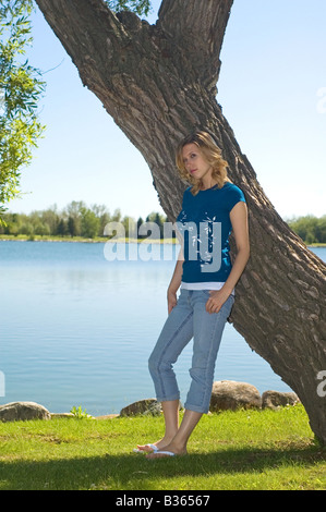 Young blonde leaning against a tree beside a lake Stock Photo