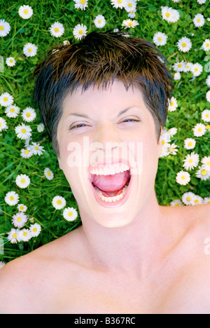Portrait of woman lying in field of daisies whilst screaming Stock Photo