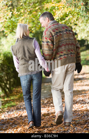 Couple outdoors walking on path in park holding hands and smiling (selective focus) Stock Photo