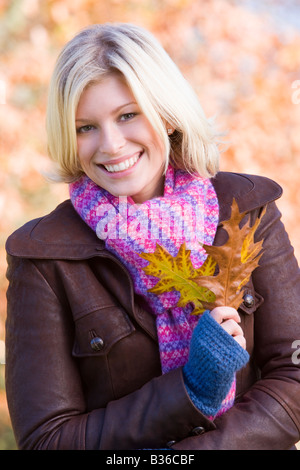 Woman outdoors at park holding leaves in hand smiling (selective focus)