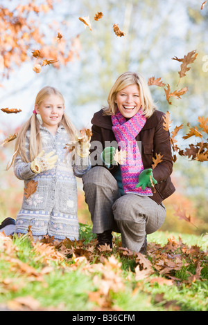Woman and young girl outdoors in park playing in leaves and smiling (selective focus)