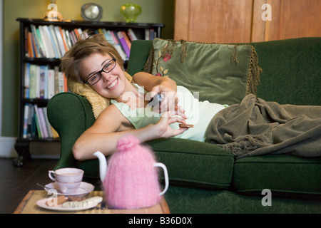 Young woman lying on sofa at home watching television Stock Photo