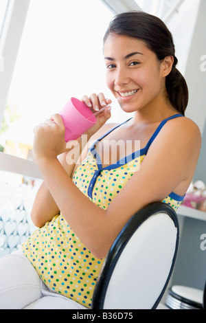 Young woman sitting by a window and having a cold drink Stock Photo