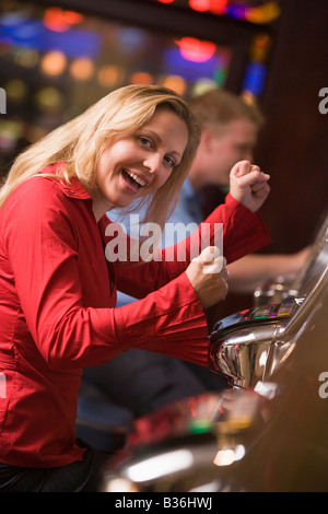 Woman in casino excited playing slot machine with people in background (selective focus) Stock Photo