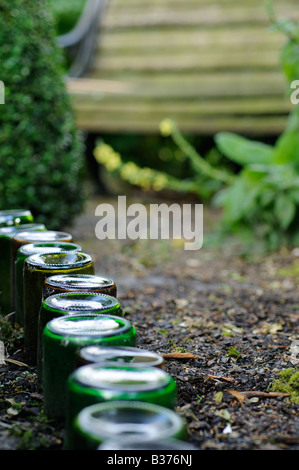 Bottles used as path edging feature in an urban garden path leading to garden seat Norfolk UK Stock Photo