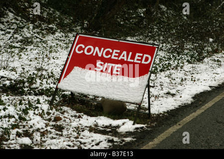Road sign covered in snow stating concealed Site Entrance Stock Photo