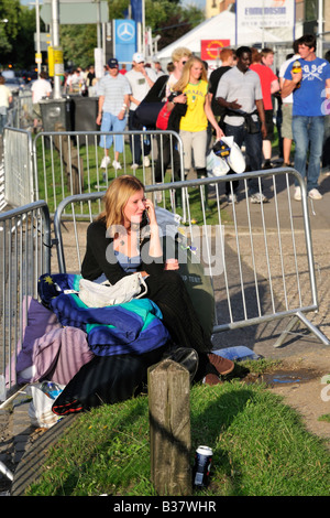 Festival goers arriving at the Reading Festival, UK, showing girl sitting on luggage on Richfield Ave on mobile phone to friends Stock Photo
