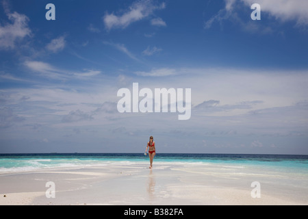 Young woman walking along deserted white sand beach surrounded by tropical waters in Maldives near India Stock Photo
