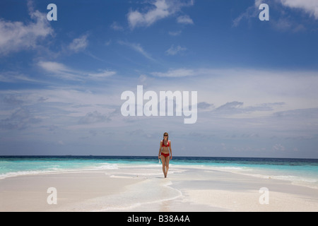 Young woman walking along deserted white sand beach surrounded by tropical waters in Maldives near India Stock Photo