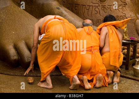 Three men pray at the feet of the statue of Lord Bahubali. Stock Photo