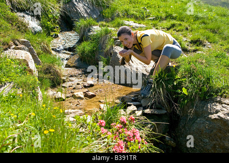 Junge Frau trinkt Wasser aus einem Bergbach, young woman drinks mountain water Stock Photo
