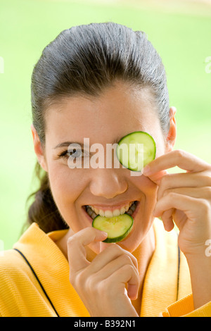 Junge Frau mit einer Gurkenscheibe vor dem Auge, Young woman with a cucumber disk before the eye Stock Photo