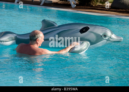 Middle aged man swimming with inflatable dolphin in swimming pool Stock Photo