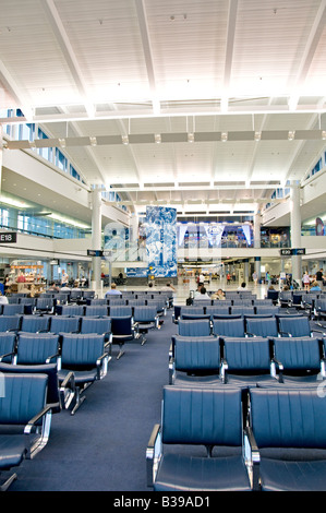 George Bush Intercontinental Airport Interior Houston Texas | HOUSTON, Texas — Rows of empty gate seating stretch through a concourse at George Bush Intercontinental Airport, its soaring skylit ceiling and open sightlines typical of the terminal's late-20th-century design. The airport, a principal hub for United Airlines following its 2010 merger with Continental, moves tens of millions of passengers annually. A Fox Sports Skybox display and mounted artwork mark the concourse's central atrium. Stock Photo