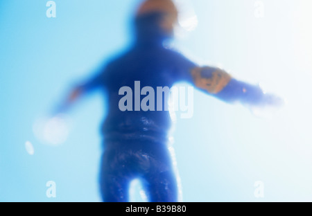 Impressionistic close up of model of skateboarder in blue gear and yellow helmet and pads leaping against blue sky Stock Photo