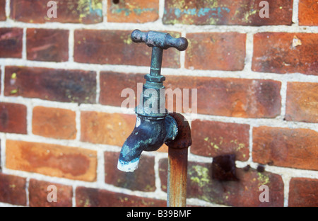 Close up of old fashioned stained outside tap fixed to rusting pipe which has come away from brickwall behind it Stock Photo